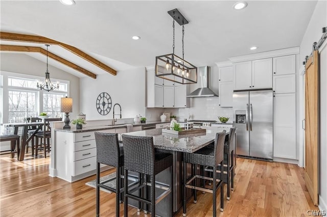 kitchen featuring light wood-type flooring, wall chimney exhaust hood, a chandelier, stainless steel fridge with ice dispenser, and a barn door