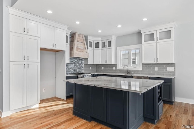 kitchen with custom range hood, light hardwood / wood-style floors, tasteful backsplash, sink, and a center island