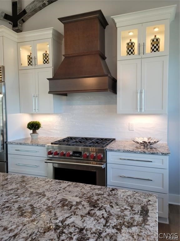 kitchen featuring luxury stove, premium range hood, decorative backsplash, and white cabinetry