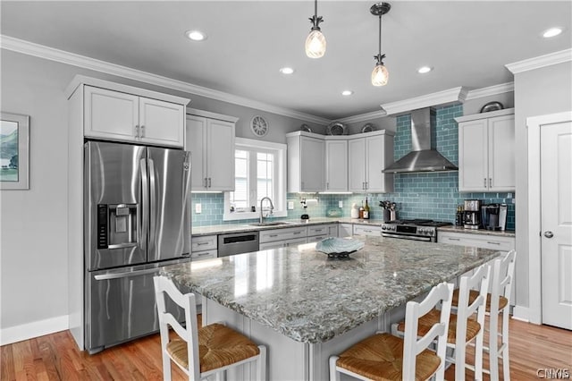 kitchen with wall chimney range hood, light hardwood / wood-style flooring, backsplash, a kitchen bar, and stainless steel appliances