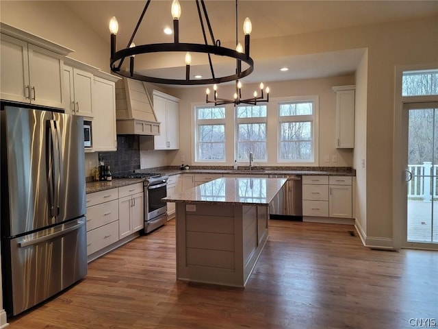 kitchen featuring appliances with stainless steel finishes, custom range hood, light stone countertops, a kitchen island, and hardwood / wood-style flooring