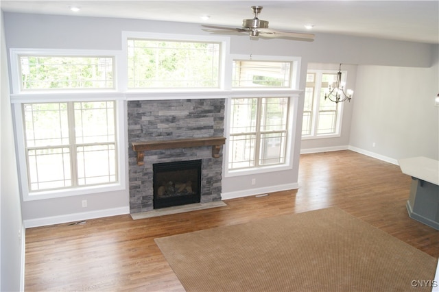 unfurnished living room featuring light hardwood / wood-style flooring, ceiling fan with notable chandelier, and a stone fireplace