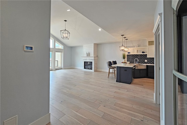 kitchen featuring a kitchen breakfast bar, hanging light fixtures, decorative backsplash, an island with sink, and a large fireplace