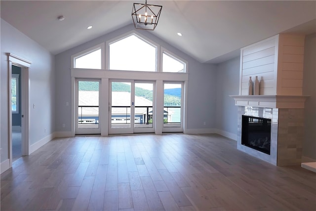 unfurnished living room with high vaulted ceiling, a chandelier, a tile fireplace, and hardwood / wood-style floors