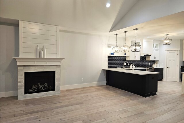 kitchen featuring decorative backsplash, white cabinetry, kitchen peninsula, light wood-type flooring, and decorative light fixtures