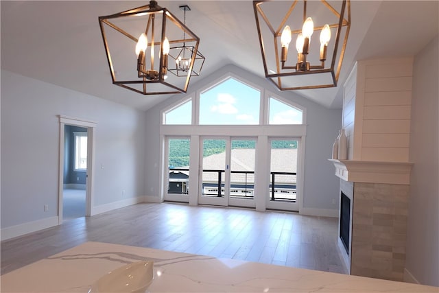 unfurnished living room featuring high vaulted ceiling, a fireplace, a chandelier, and hardwood / wood-style flooring