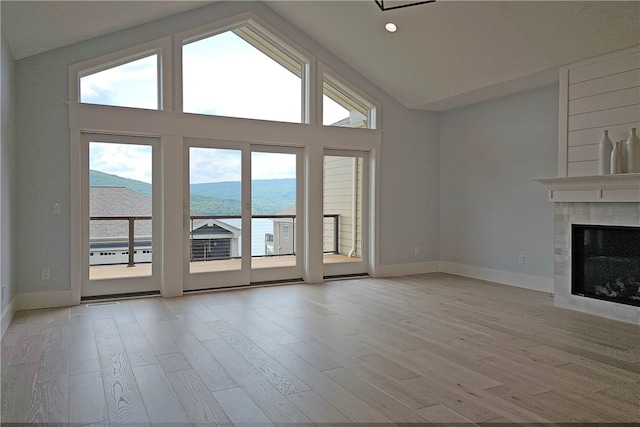 unfurnished living room with a fireplace, light hardwood / wood-style flooring, a mountain view, and high vaulted ceiling