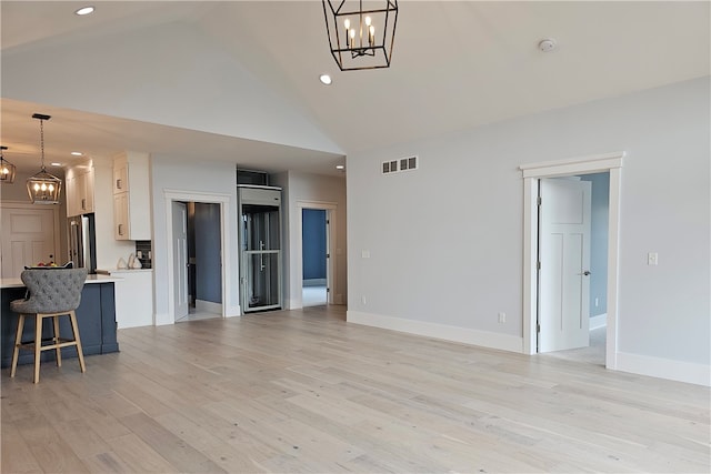 unfurnished living room with high vaulted ceiling, light hardwood / wood-style flooring, and a chandelier