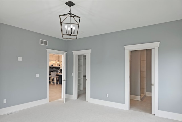 unfurnished bedroom featuring light colored carpet, a notable chandelier, ensuite bathroom, and a spacious closet