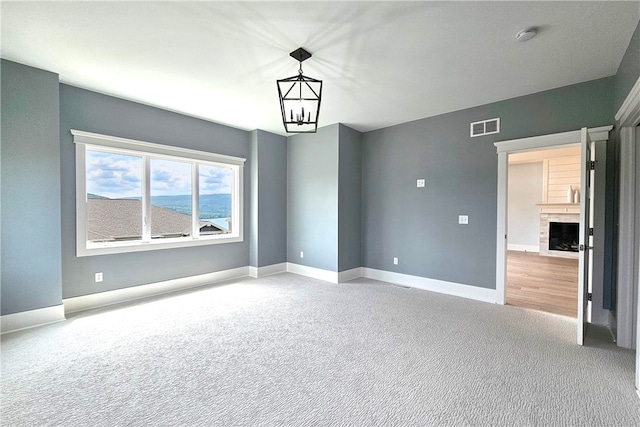 carpeted spare room featuring a chandelier and a fireplace