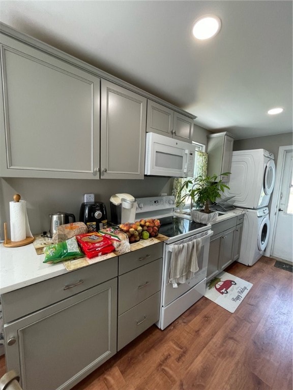 kitchen featuring white appliances, gray cabinets, stacked washer and dryer, and hardwood / wood-style flooring