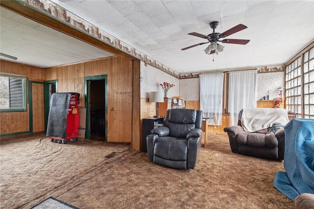 carpeted living room featuring wooden walls and ceiling fan