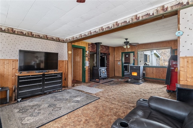 carpeted living room featuring a wood stove, wooden walls, and ceiling fan