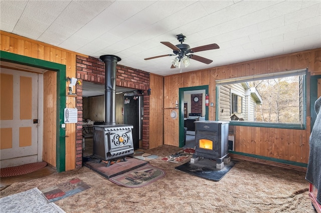 interior space featuring ceiling fan, wood walls, a wood stove, and dark colored carpet