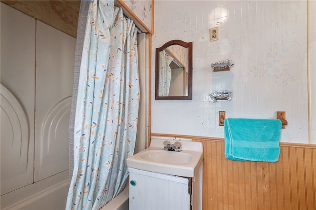 bathroom with shower / bath combo with shower curtain, wood walls, and vanity