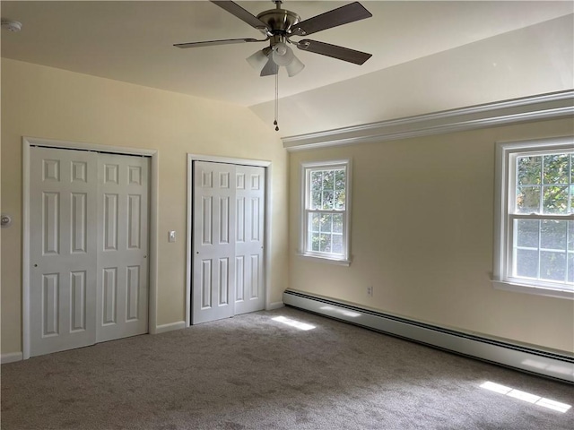 unfurnished bedroom with multiple windows, carpet flooring, two closets, and baseboard heating