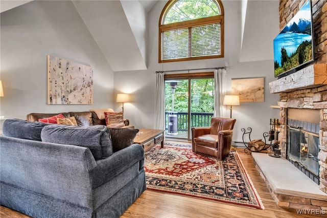 living room featuring high vaulted ceiling, hardwood / wood-style floors, and a stone fireplace