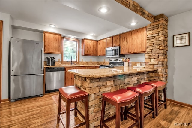 kitchen with sink, light hardwood / wood-style flooring, light stone counters, stainless steel appliances, and kitchen peninsula