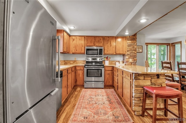 kitchen with a breakfast bar, light hardwood / wood-style flooring, light stone counters, stainless steel appliances, and kitchen peninsula