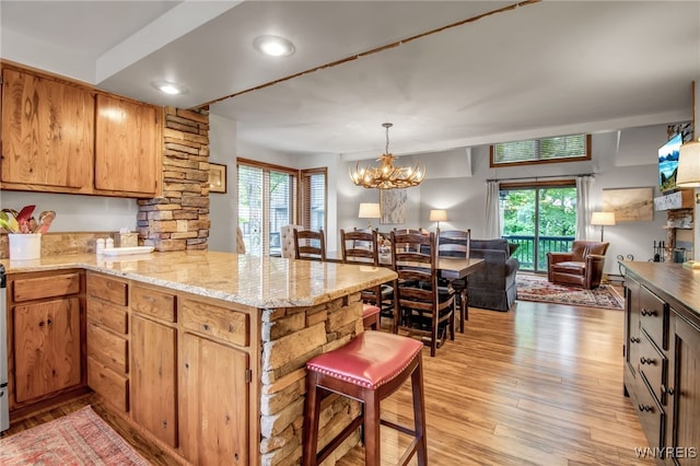 kitchen featuring hanging light fixtures, an inviting chandelier, light hardwood / wood-style flooring, light stone countertops, and kitchen peninsula