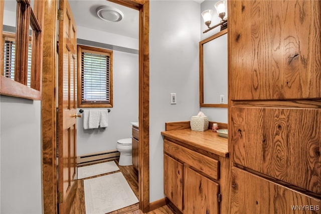 bathroom with hardwood / wood-style flooring, baseboard heating, vanity, and toilet