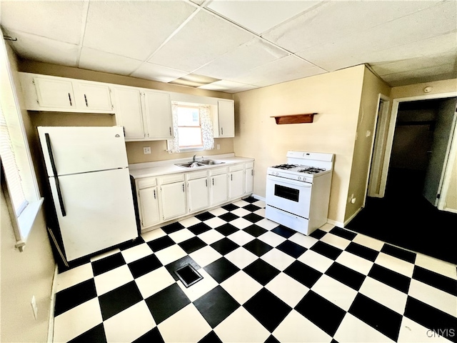 kitchen featuring dark tile patterned floors, white cabinetry, sink, a drop ceiling, and white appliances