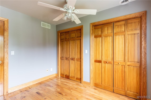 unfurnished bedroom featuring ceiling fan, light wood-type flooring, and multiple closets