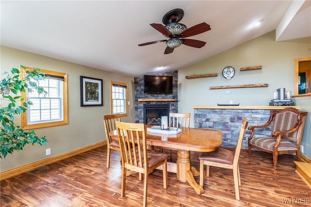 dining room with ceiling fan, vaulted ceiling, a stone fireplace, and wood-type flooring