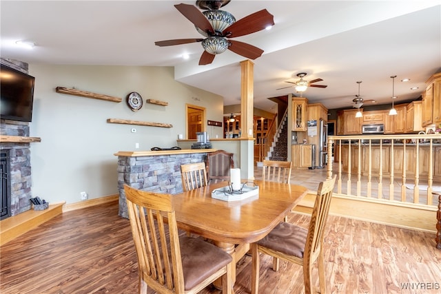 dining area with light wood-type flooring, lofted ceiling, ceiling fan, and a fireplace