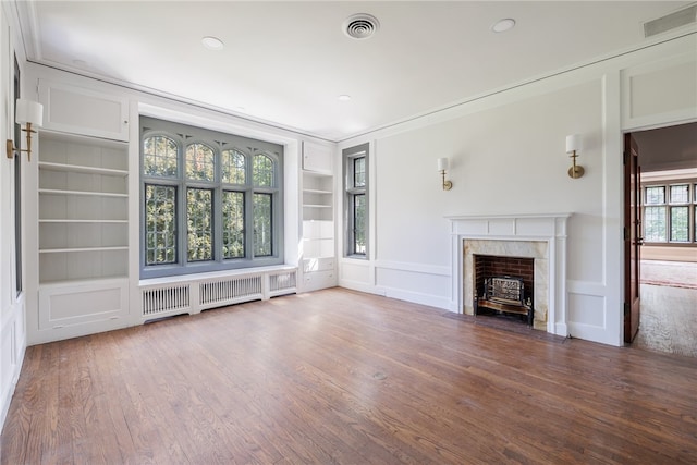 unfurnished living room with a healthy amount of sunlight, wood-type flooring, radiator heating unit, and built in shelves