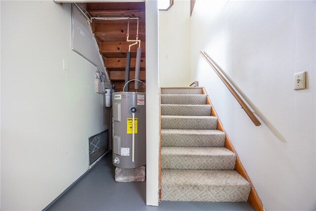 staircase featuring electric water heater and concrete floors