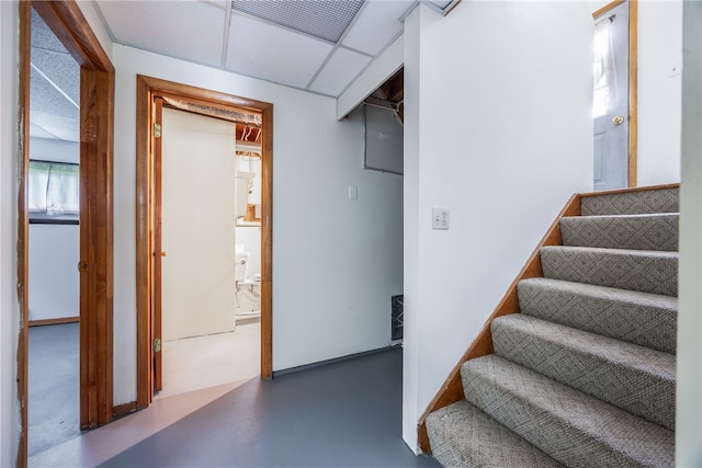 staircase featuring concrete floors and a drop ceiling