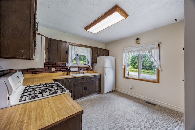 kitchen featuring dark brown cabinetry, light carpet, white fridge, sink, and stove