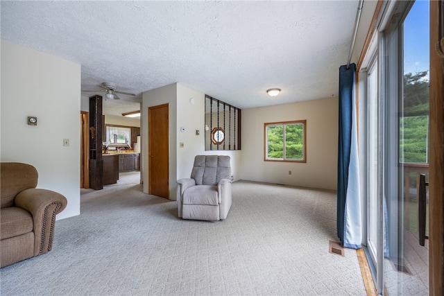 sitting room with ceiling fan, a textured ceiling, and light carpet