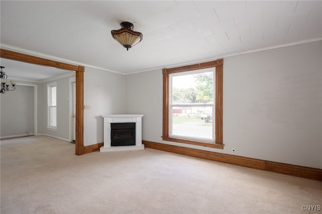 unfurnished living room with a notable chandelier, light carpet, baseboards, ornamental molding, and a glass covered fireplace