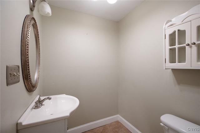 half bath featuring toilet, tile patterned flooring, baseboards, and a sink