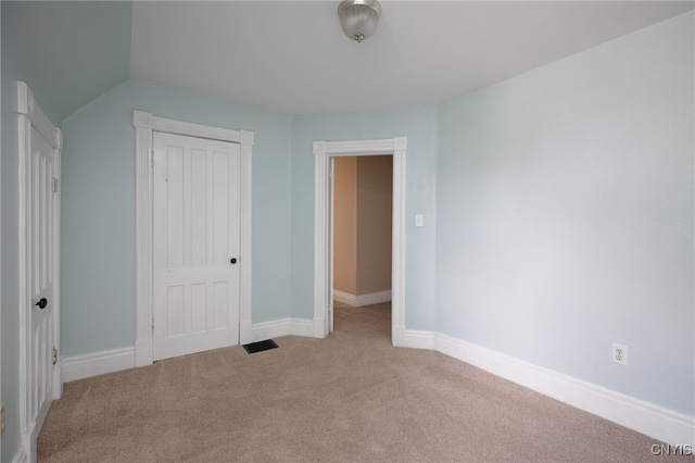 unfurnished bedroom with baseboards, visible vents, light colored carpet, vaulted ceiling, and a closet