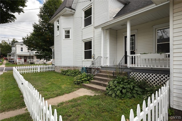 exterior space with a shingled roof, fence, a porch, and a lawn