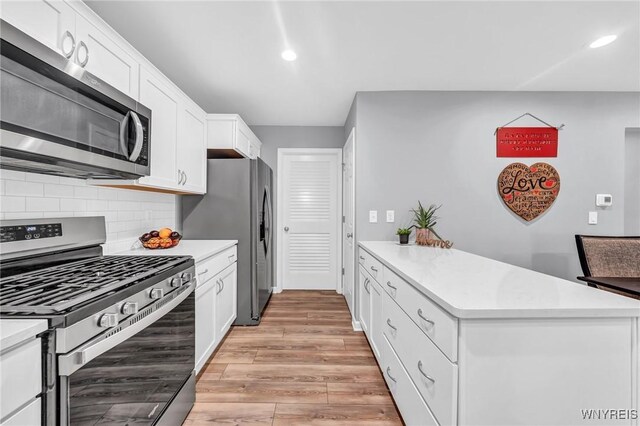 kitchen with white cabinets, kitchen peninsula, light hardwood / wood-style flooring, appliances with stainless steel finishes, and decorative backsplash