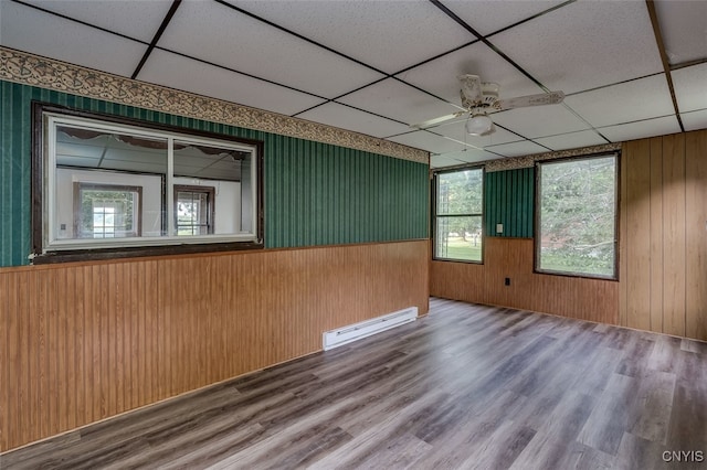 unfurnished room with ceiling fan, a baseboard heating unit, a paneled ceiling, and wood-type flooring