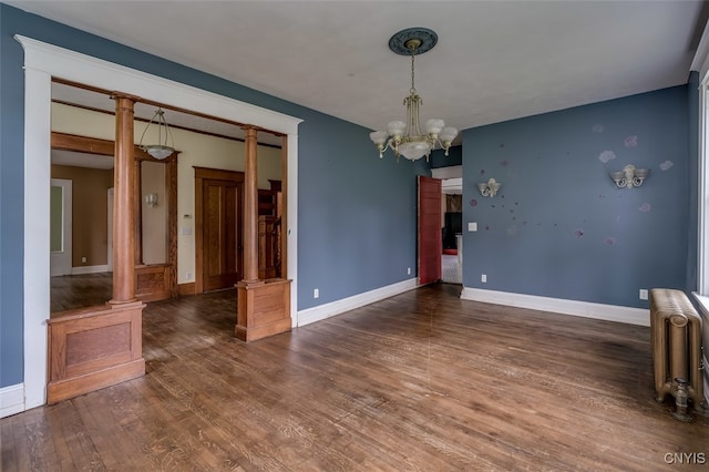 spare room featuring ornate columns, dark wood-type flooring, and a chandelier