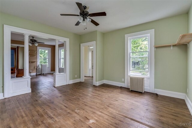 unfurnished room featuring ceiling fan, hardwood / wood-style flooring, ornate columns, and radiator