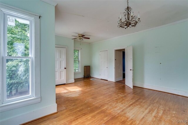 empty room with light hardwood / wood-style flooring, ceiling fan with notable chandelier, a healthy amount of sunlight, and ornamental molding