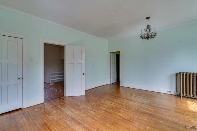 unfurnished room with crown molding, radiator heating unit, light hardwood / wood-style floors, and a chandelier