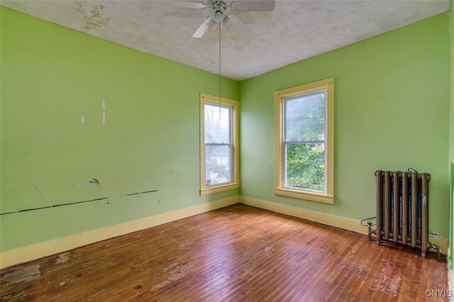 empty room with ceiling fan, hardwood / wood-style flooring, and radiator heating unit