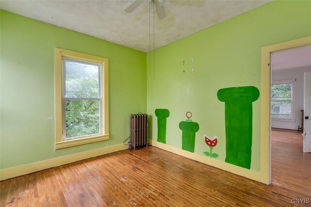 spare room featuring ceiling fan, radiator heating unit, a healthy amount of sunlight, and wood-type flooring