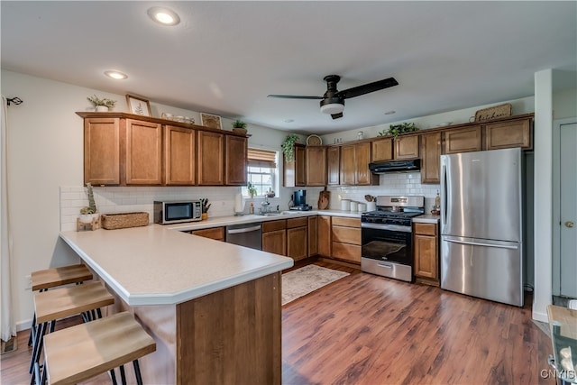 kitchen featuring backsplash, dark wood-type flooring, ceiling fan, stainless steel appliances, and kitchen peninsula