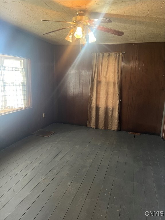 empty room with wood walls, hardwood / wood-style flooring, and ceiling fan