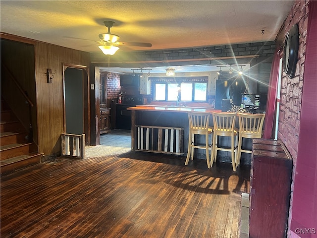 interior space featuring ceiling fan, dark wood-type flooring, indoor bar, and brick wall