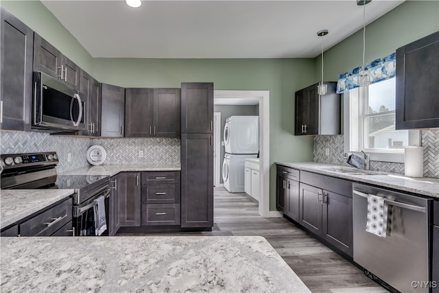 kitchen with stacked washing maching and dryer, stainless steel appliances, decorative backsplash, sink, and wood-type flooring